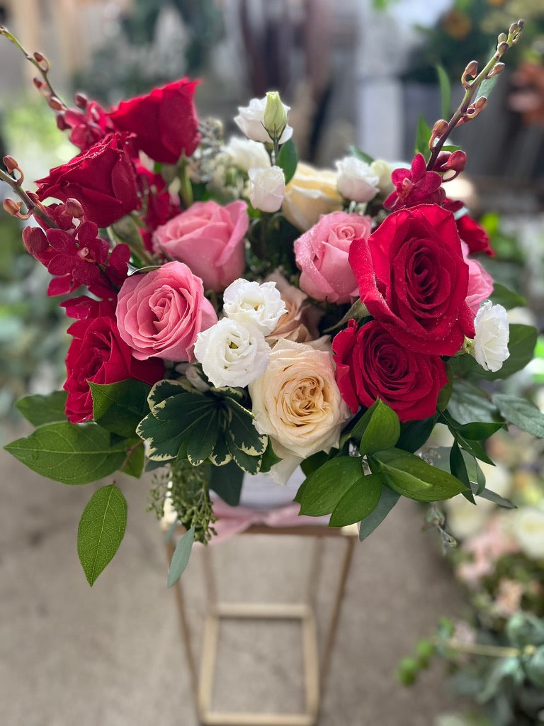 Bouquet of red, pink, and white roses with green leaves in a metal basket.