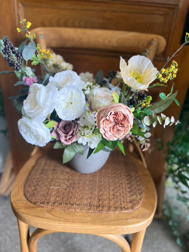 Floral arrangement in a white vase on a wooden chair with a blurred background