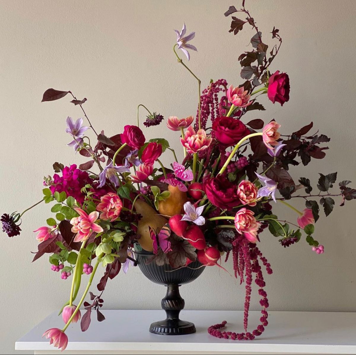 Antique black vase filled with a generous amount of colourful flowers and fruit