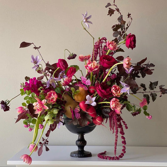 Antique black vase filled with a generous amount of colourful flowers and fruit