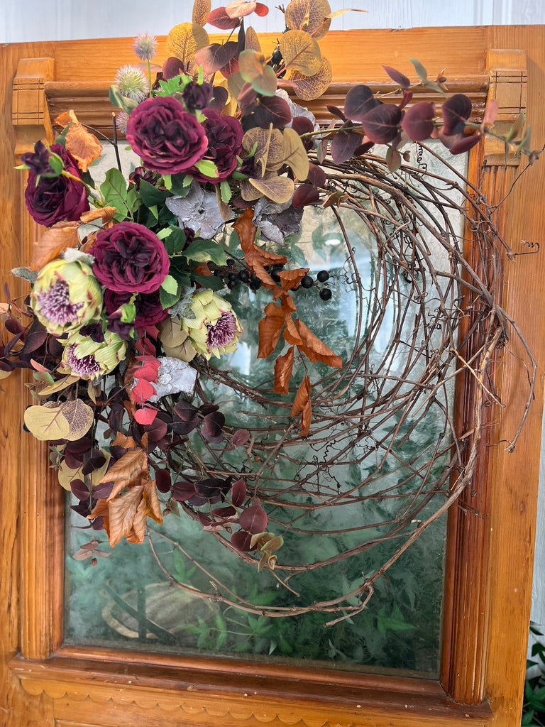 Natural grapevine entwined with fall toned garden style flowers in a crescent shape